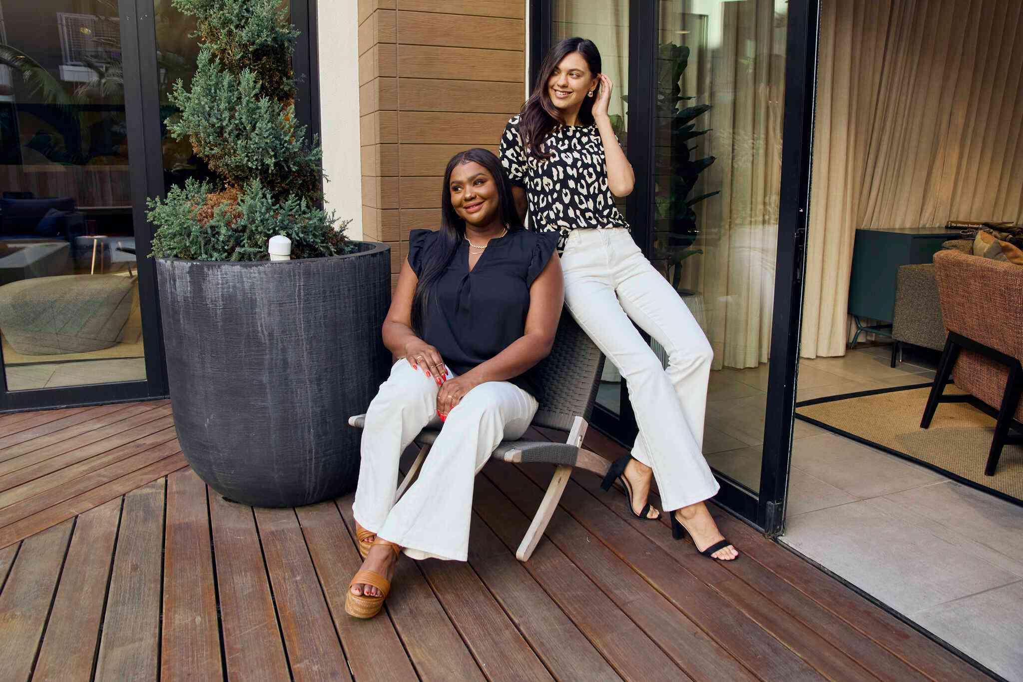 Two women sitting on a wooden deck with a plant in the background.