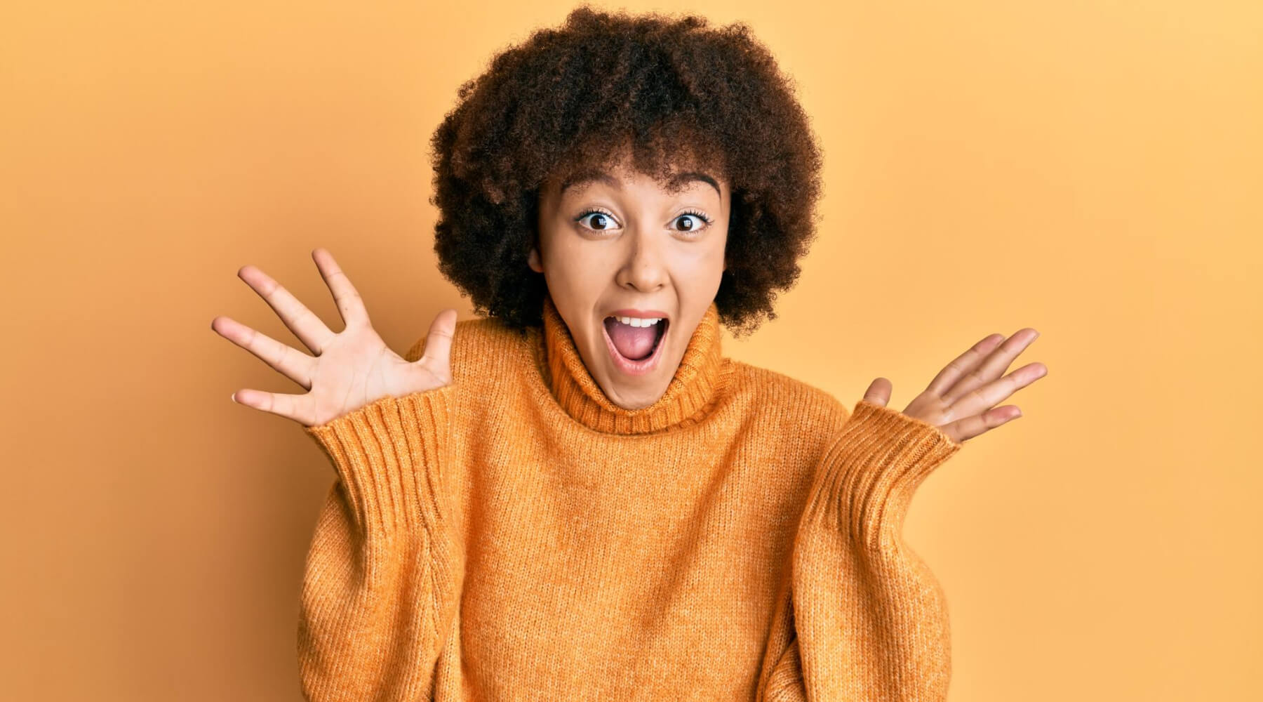 A woman in an orange sweater, looking surprised with wide eyes and an open mouth.