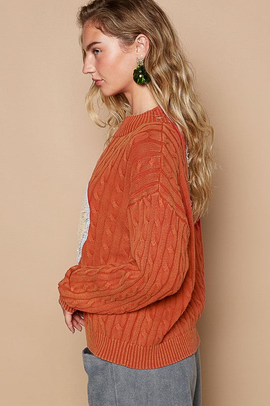 Side view of orange cable-knit sweater with peace patch