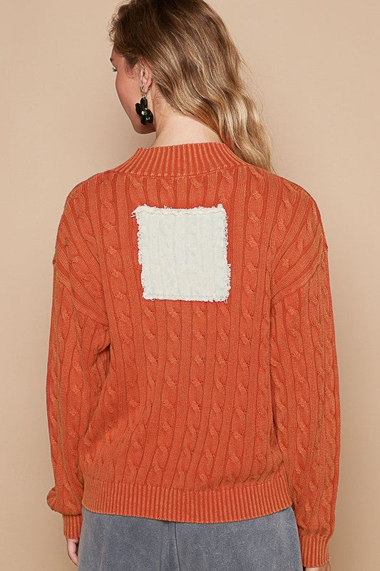 Back view of orange cable-knit sweater with square patch