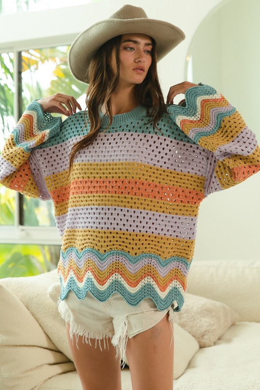 Colorful crochet sweater with wavy hem, worn by model in hat.