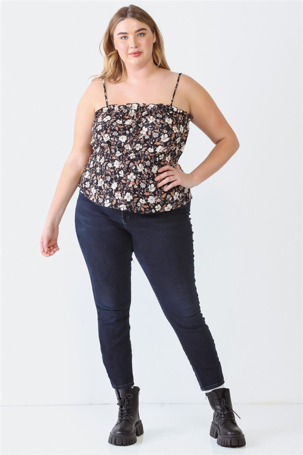 A woman stands against a plain backdrop, wearing a Plus Size Cami | Zenobia Frill Floral Square Neck, dark jeans, and black boots.